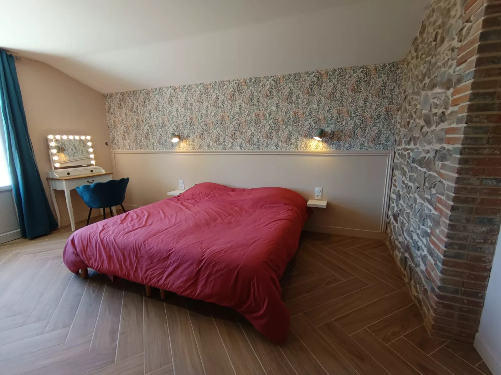 La chambre nuptiale : grand lit, mur de pierre et de brique apparent, papier peint fleuri