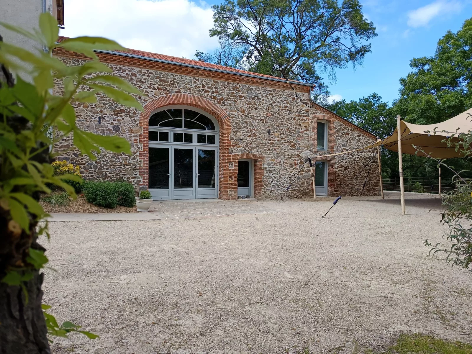 La salle de réception du Moulin de la Noue Ronde vue de l'extérieur : façade de pierre, grande porte vitrée cintrée et cour gravillonnée